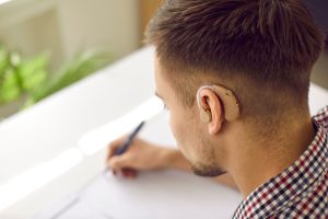Person writing notes while adjusting to wearing and listening with hearing aids.
